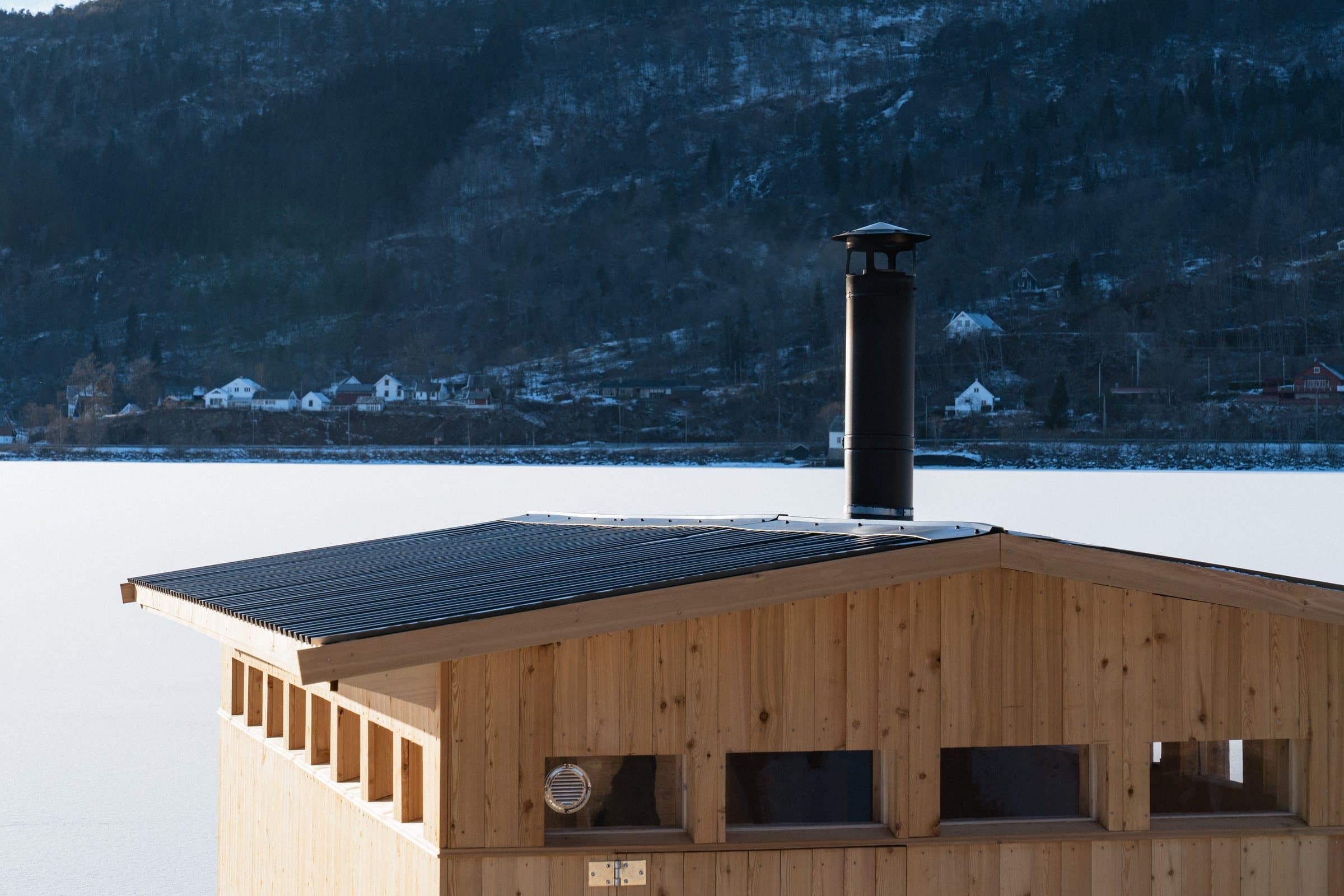 Saunaen sett frå sida, med pipa og fjorden bak
